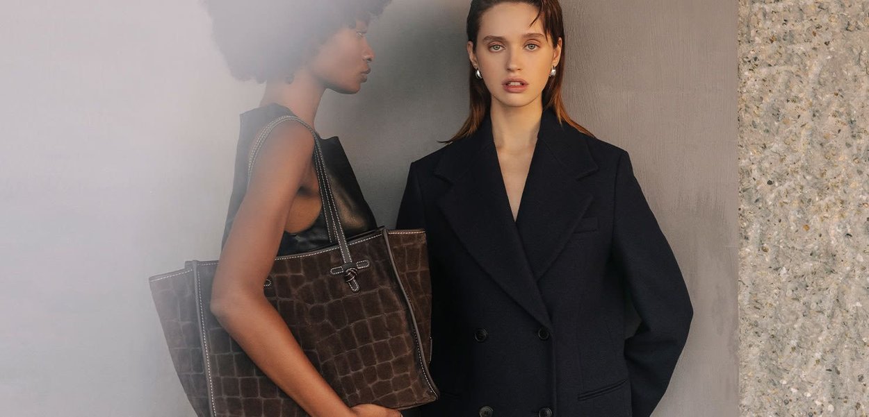 Braune Tasche mit Krokodilstruktur und silbernem Metall. Zwei Modelle: eines in einem schwarzen ärmellosen Oberteil und das andere in einem marineblauen doppelt geknöpften Blazer.