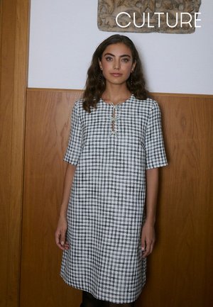 Schwarz-weiß kariertes Kleid mit rundem Ausschnitt, kurzen Ärmeln und einer vorderen Schnürung. Der Stoff hat eine strukturierte Oberfläche.