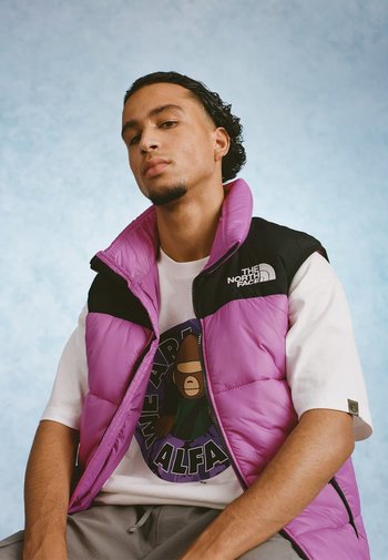 Paarse gewatteerde vest met zwarte accenten, voorzien van een hoge kraag en een ritssluiting, gelaagd over een witte graphic t-shirt. Zachte textuur.