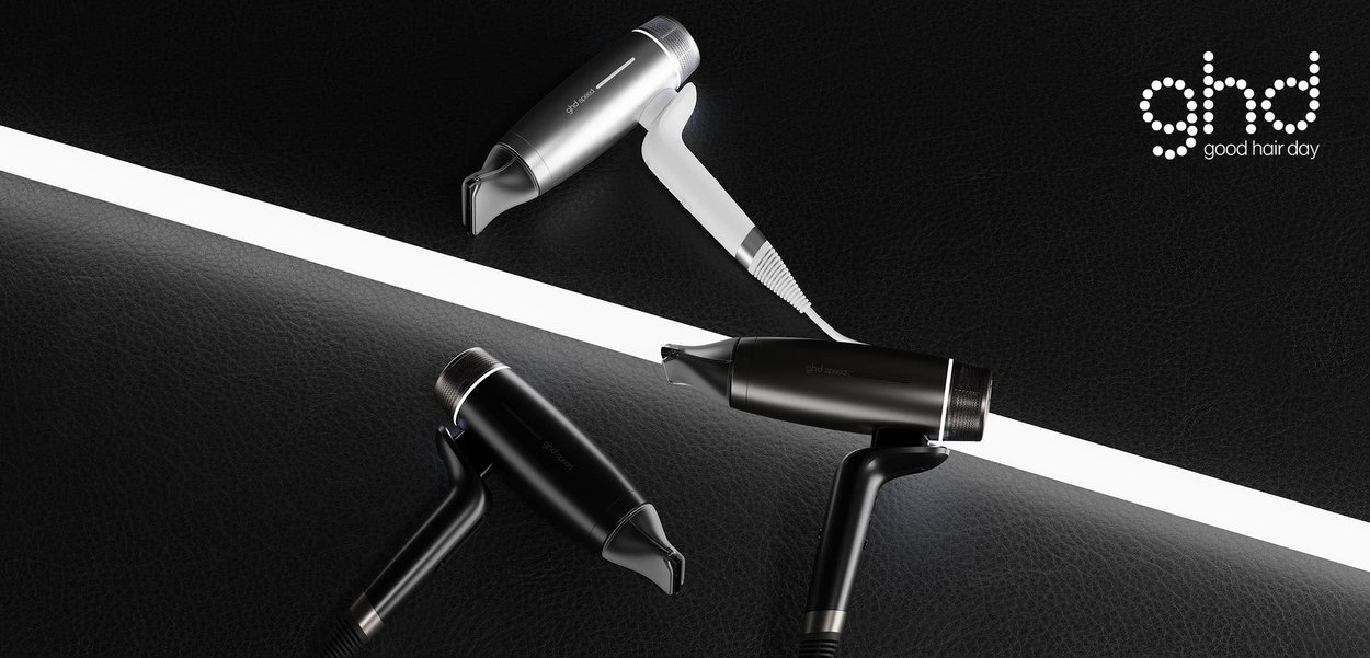 Trzy suszarki do włosów GHD w kolorze czarnym i srebrnym ułożone na czarnej teksturowanej powierzchni, z logo GHD w prawym górnym rogu.