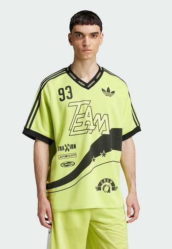 Neon groene oversized trui met zwarte accenten, voorzien van "TEAM" grafiek, logo's en diverse teksten. Korte mouwen en een ronde halslijn.