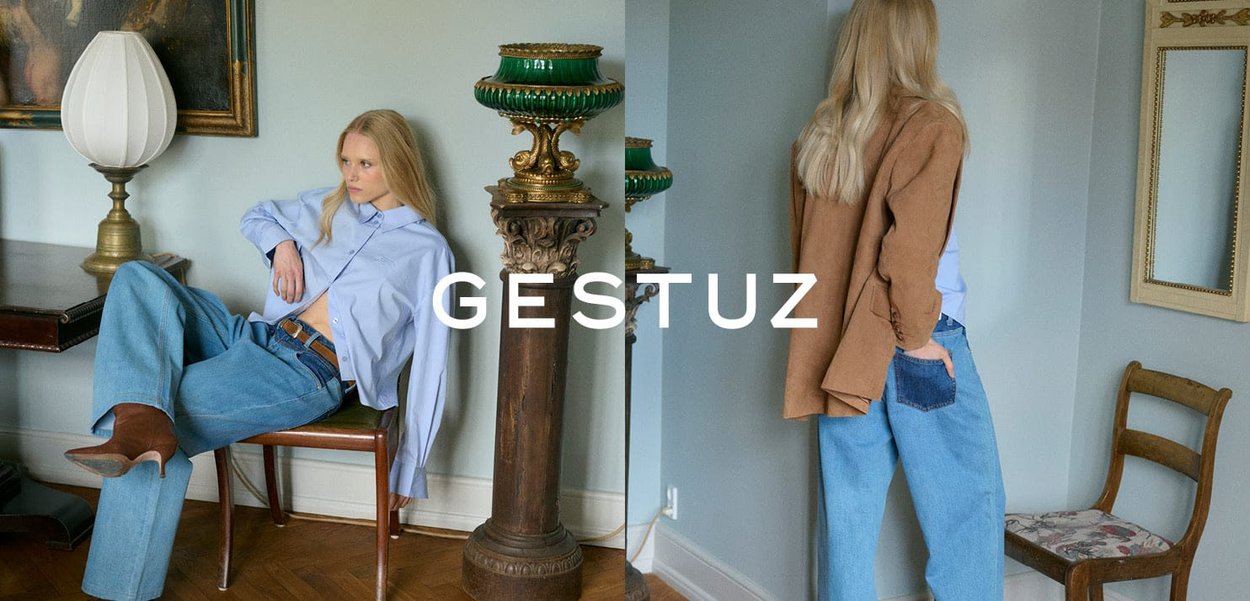 Blauw shirt, bruine blazer, wijde jeans en bruine laarzen. Zachte texturen, neutrale kleuren en eenvoudige ontwerpen, met een decoratieve lamp op de achtergrond.