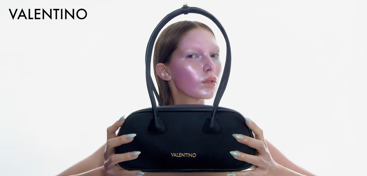 Czarna skórzana torebka o usztywnionym kształcie, z dwoma zaokrąglonymi uchwytami i złotym logo. Modelka trzyma torebkę na białym tle.