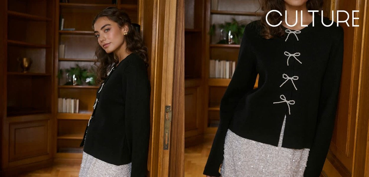 Schwarzer Strickcardigan mit perlenverzierten Schleifenverschlüssen, langen Ärmeln und einem Seitenschlitz. Gestylt über einem glänzenden silbernen Kleid, drinnen aufgenommen.