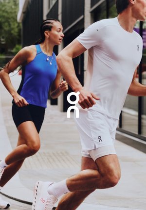 Deux coureurs sur un chemin, portant des vêtements de sport. La femme porte un débardeur bleu et un short noir ; l'homme est en chemise blanche et en short. Tous deux portent des chaussures de course.
