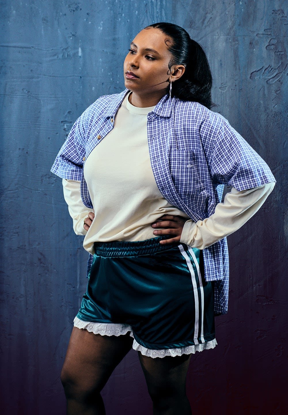 Modelis vilki mėlyną languotą marškinėlį virš baltų ilgomis rankovėmis marškinių, derindamas su žaliais satino šortais, kuriuose yra balti nėriniai ir šoninės juostos.