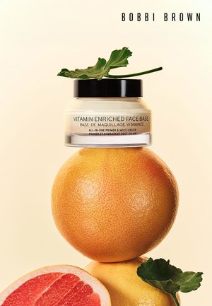 Crème de visage enrichie en vitamines de Bobbi Brown dans un pot avec un couvercle noir, posée sur un pamplemousse, avec une touche de feuille verte et une texture crémeuse lisse.