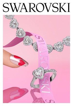 Anello e bracciale a forma di cuore in cristallo su sfondo rosa, con un nastro rosa Swarovski e una mano con nail art a forma di cuore.