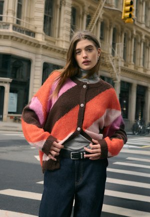 Cardigan en tricot avec une coupe oversize ; présente des rayures diagonales vives en orange, marron, rose et violet ; fermeture à boutons à l'avant ; texture douce.