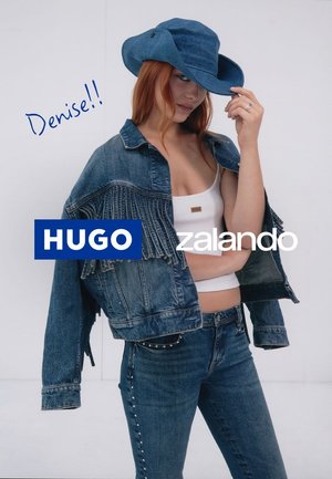 Jeansjacke mit Fransen, kombiniert mit einem weißen Cropped-Top und enganliegenden Jeans mit Nietenakzenten. Eine passende Denim-Mütze rundet den Look ab.