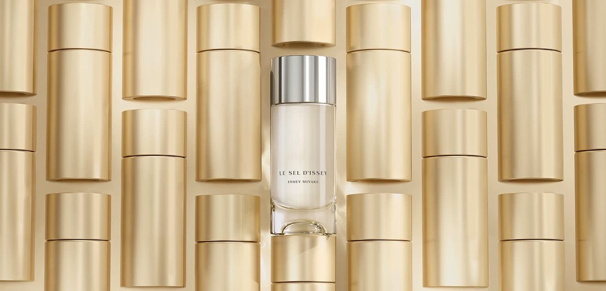 Bottiglia di profumo in vetro con tappo argento, circondata da contenitori cilindrici dorati, caratterizzata da un design pulito e una texture liscia.