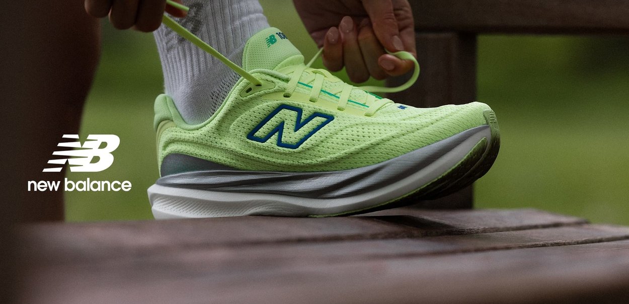 Osoba zawiązująca neonowożółty but do biegania New Balance z zielonymi i niebieskimi akcentami, opierająca stopę o drewnianą ławkę na zewnątrz.