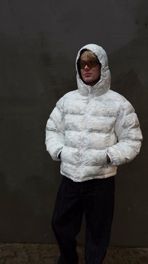 Doudoune blanche avec un motif camouflage subtil, fermeture éclair, col montant et deux poches avant. Portée avec un jean foncé.