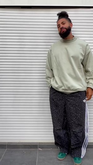 Hellgrüner übergroßer Pullover, schwarze Leoparden-Print-Hose mit weißen Streifen und grüne Sneaker. Glatte Textur, lässige Passform.