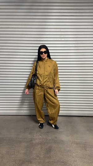 Chándal de bronce con chaqueta con cremallera y cinturilla elástica; combinado con zapatillas negras. Accesorio: bolso negro. Textura suave.