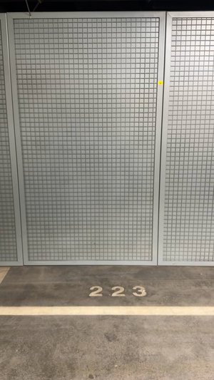 Clôture en métal argenté avec un motif de maillage carré, présentant le numéro "223" marqué sur le sol en béton beige.