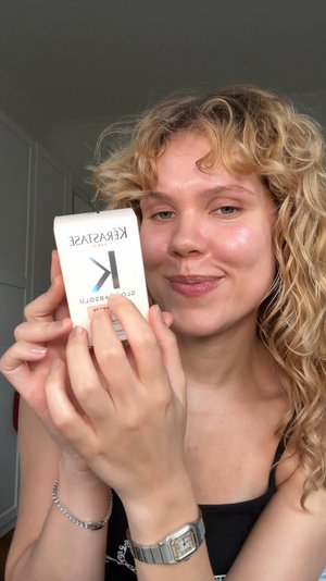 Kérastase product box in cream with metallic logo. Box features a cut-out design on top and is held in a hand with silver jewelry.