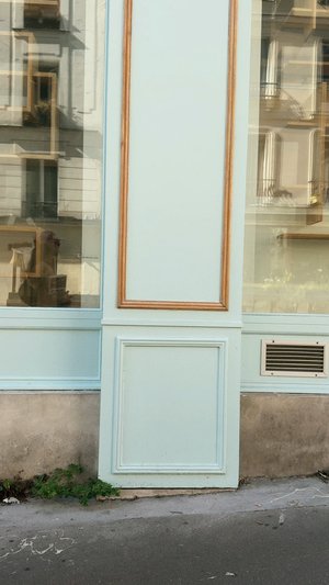 Light blue wall with wooden accents and decorative paneling; large glass window reflects surrounding buildings; visible air vent at the bottom.