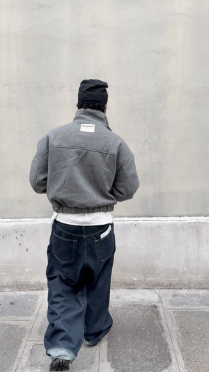 Veste polaire grise avec col montant et ourlet élastique, associée à un pantalon en denim foncé. Étiquette patch remarquable à l'arrière de la veste.