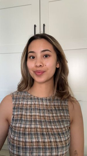 Bruin en blauw geruite mouwloze top met verzamelde textuur; gladde stof, lichte glans; model met lang, golvend haar tegen een neutrale achtergrond.