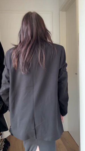 Schwarze maßgeschneiderte Blazer mit lockerer Passform, strukturierter Stoff, leicht verlängertem Rücken und sauberen Nähdetails. Getragen über einem figurbetonten Outfit.