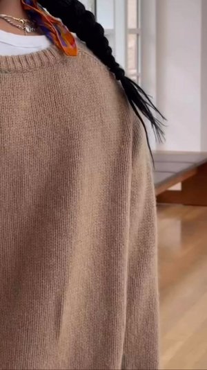 Pull en tricot oversized marron clair avec un col côtelé, présentant une texture douce. Accompagné d'une écharpe colorée nouée dans les cheveux.