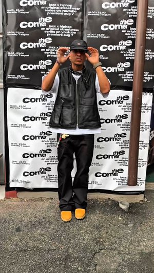 Melna ādas veste pāri balta krekla, melnas bikses un dzeltenas kurpes. Fons veido atkārtoti melni un balti pasākumu afišu motīvi.