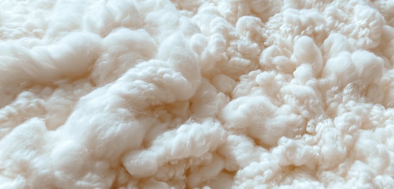Flauschiges, weißes Material mit einer weichen, wolkenartigen Textur, das zahlreiche, kugelige Stränge und eine unregelmäßige Oberfläche aufweist, die an Zuckerwatte erinnert.