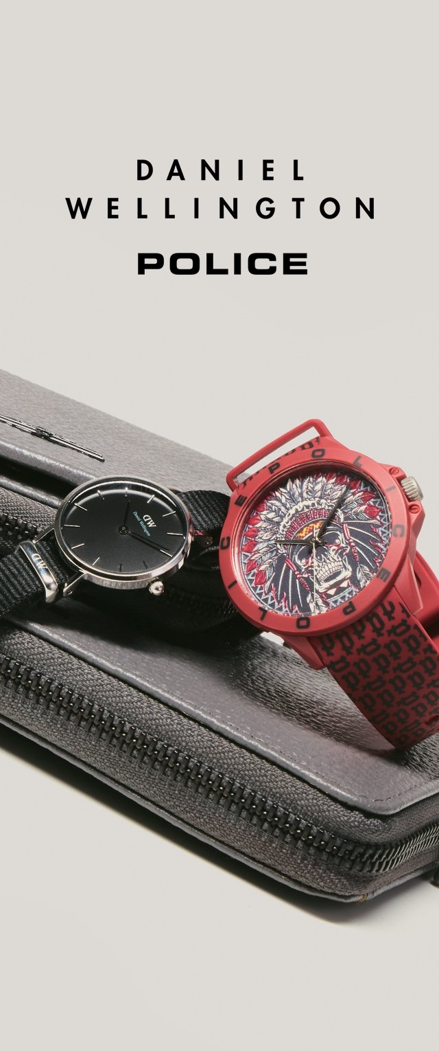 Dos relojes de pulsera, uno negro con diseño minimalista y otro rojo con patrón de calavera y tocado de plumas, colocados sobre una bolsa gris con cremallera.