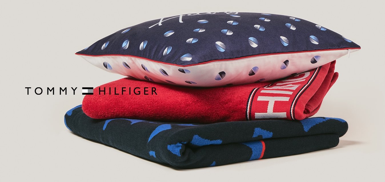 Stoh tří složených textilií: dole modrá látka s vzorem, uprostřed červená látka s bílým textem, nahoře modrý polštář s bílými a růžovými tečkami.