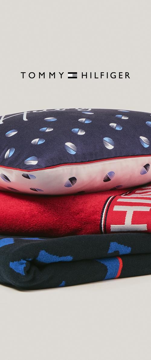 Tommy Hilfiger-kussen met marineblauwe stof, blauw-wit patroon; gestapelde gevouwen rode en zwarte kledingstukken met contrasterende kleuren en patronen.