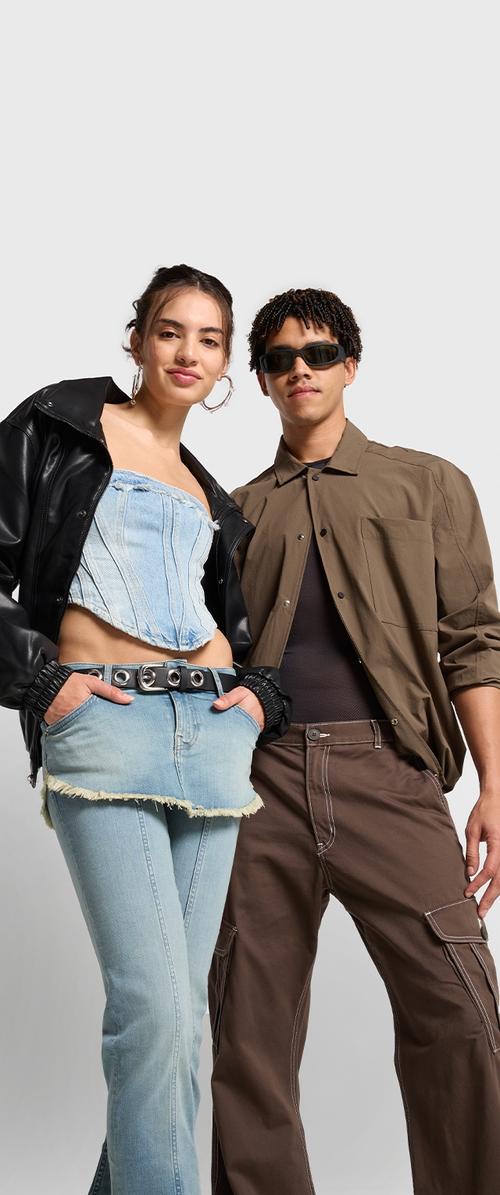 Dva posameznika nosita sodobne obleke: črno usnjeno jakno, denim crop top, zbledele svetlo modre kavbojke s frufi, in rjave cargo hlače z žepi.