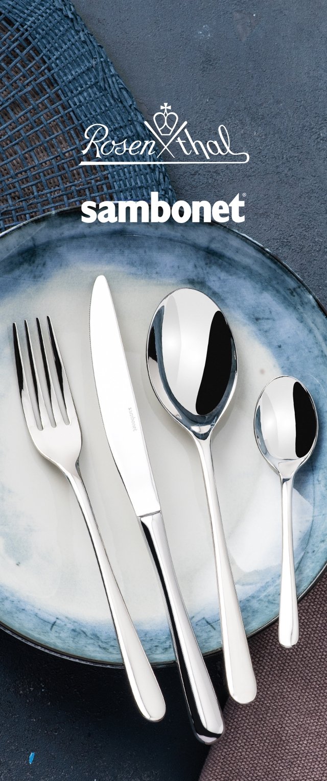 Tenedor, cuchillo, cuchara grande y cuchara pequeña sobre un plato de cerámica azul y blanca, con fondo de tapete tejido y superficie texturizada.