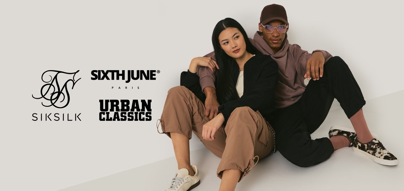 Muž a žena sedící na podlaze, opírající se o sebe, oblečení v ležérním oblečení v neutrálních tónech a s teniskami.