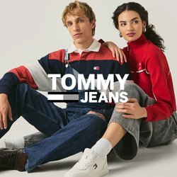 Muž v pruhovaném tričku a džínových laclích sedí vedle ženy v červeném tričku s dlouhým rukávem a šedých kalhotách na jednobarevné bílé podlaze.