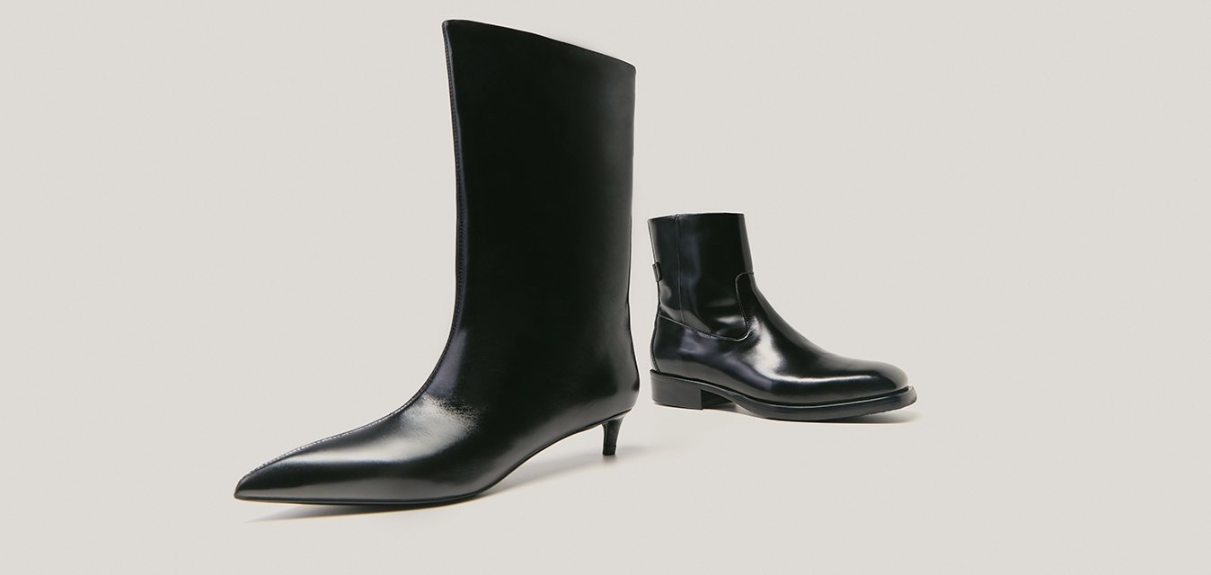 Dvoje černých kožených bot izolovaných na světlém pozadí; jedny vysoké s špičatou špičkou a kitten heel, druhé krátké kotníkové boty s plochou podrážkou.