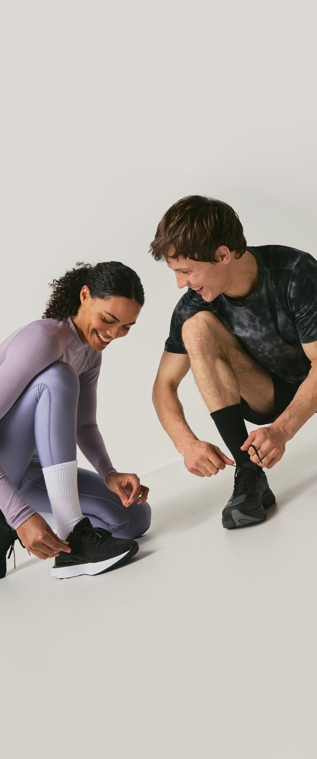 Zapatos deportivos negros con suelas blancas, usados por una persona con una camiseta negra con estampado y otra con una camiseta de manga larga morado claro y leggings.