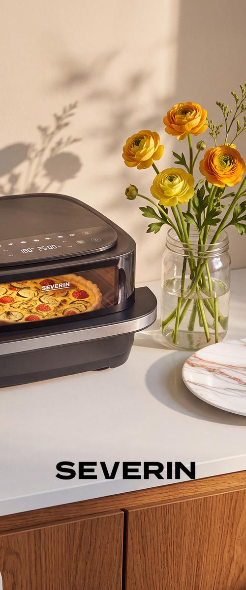 Digitaalinen pöytätasouuni paistaa kasvistäytteistä pizzaa lasipurkin vieressä, jossa on oransseja ja keltaisia rannikuksen kukkia keittiötasolla.