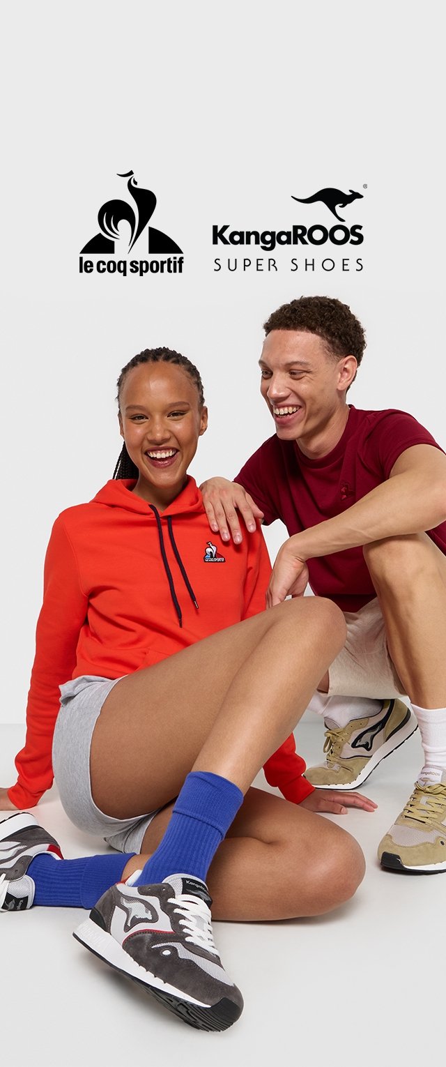Zwei Personen sitzen auf dem Boden und tragen KangaROOS Sneakers. Eine Person trägt einen leuchtend roten Hoodie und graue Shorts; die andere trägt ein bordeauxrotes T-Shirt und Shorts.