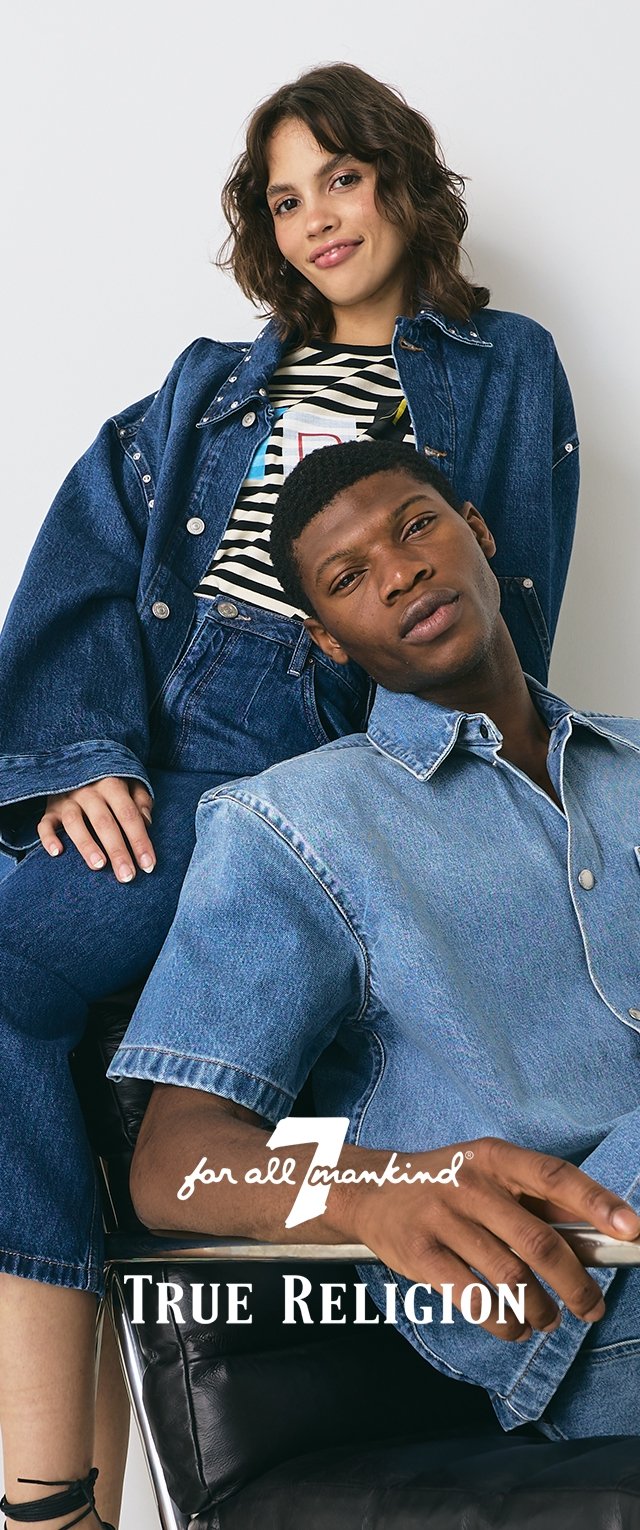 Lichtblauwe spijkerjacket en -hemd, gedragen over een gestreept shirt en blauwe overall door twee modellen die op een zwarte stoel zitten. Merklogo zichtbaar.