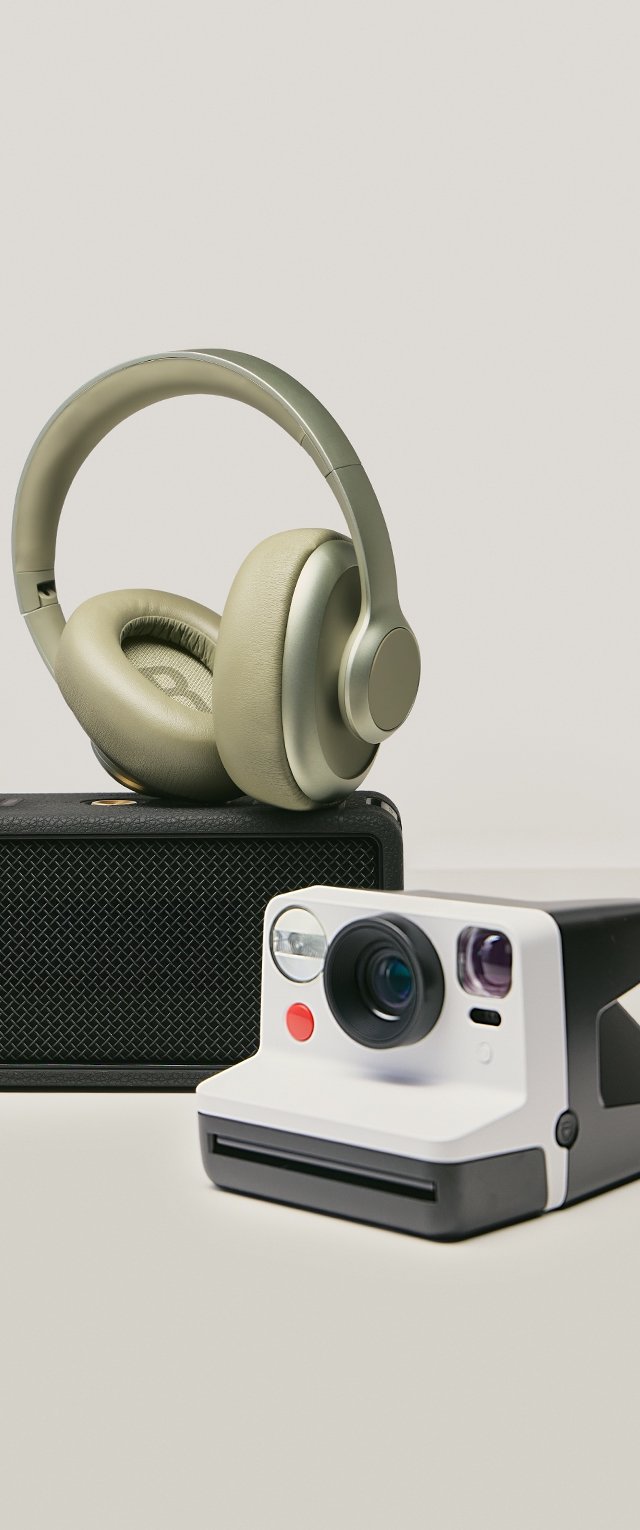 Des écouteurs sans fil en olive, un haut-parleur portable noir avec une finition texturée, et un appareil photo instantané noir et blanc avec un objectif rond.