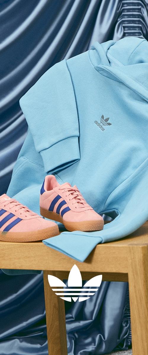 Hellblaue Kapuzenjacke mit silbernem Logo liegt neben rosa Turnschuhen mit blauen Streifen und einer strukturierten Gummisohle auf einem Holztisch.