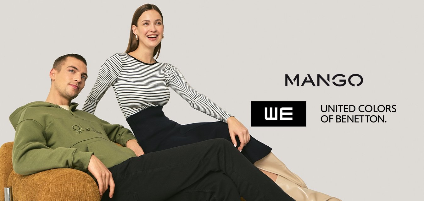 Muž v zelené mikině s kapucí se opírá na hnědém křesle, žena v pruhovaném topu a černé sukni sedí vedle něj, oba se usmívají na jednobarevném pozadí.