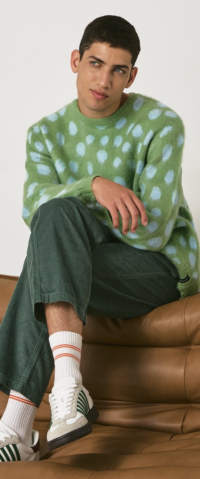 Suéter verde esponjoso con lunares azul claro, combinado con pantalones de pana verde oscuro y zapatillas blancas con rayas verdes y acentos naranjas.