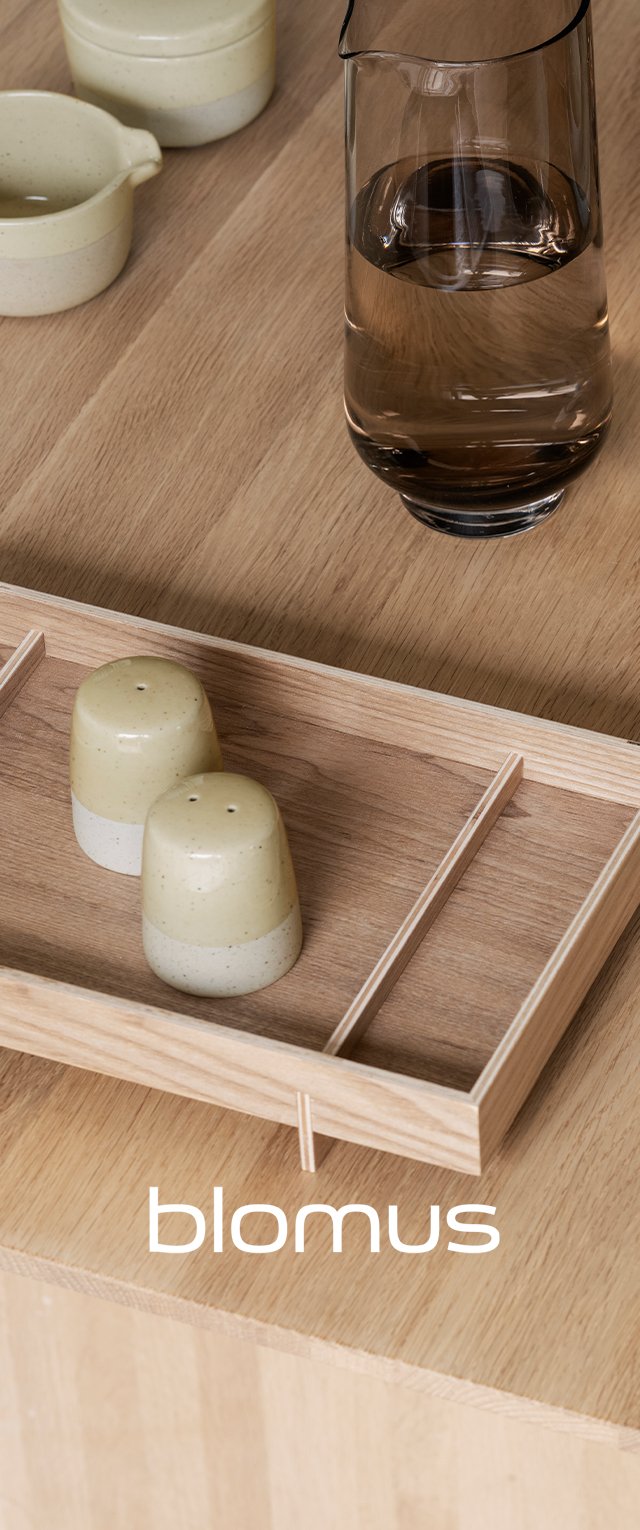 Holztablett mit zwei grün gefleckten keramischen Salz- und Pfeffermühlen; neben ihnen steht eine klare Glaskanne mit Wasser auf einer Holzoberfläche.