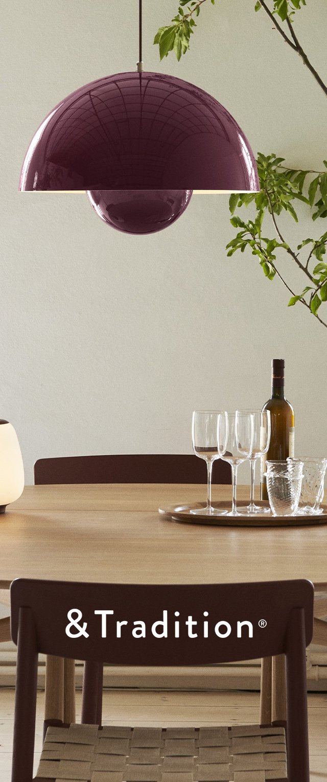 Lámpara colgante glossy de color púrpura con diseño esférico, suspendida sobre una mesa de madera. Incluye cristalería y una botella de vino como parte del entorno.