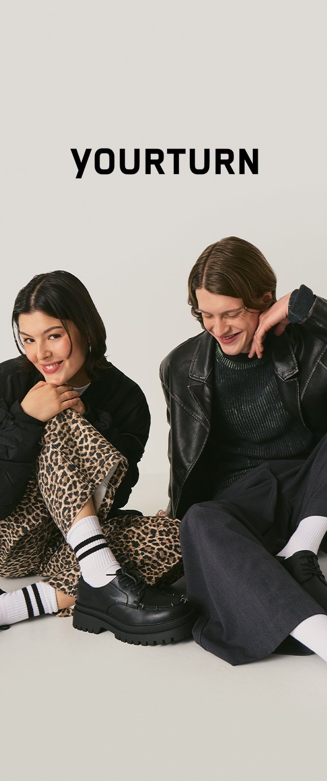 Zapatos de cuero negros, pantalones con estampado de leopardo, suéter oscuro con textura y chaqueta acolchada. Medias a rayas realzan el atuendo casual.