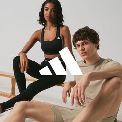 Dva mladí dospělí v sportovním oblečení sedí u dřevěných laviček v minimalistickém interiéru, oba mají na nohou tenisky Adidas.