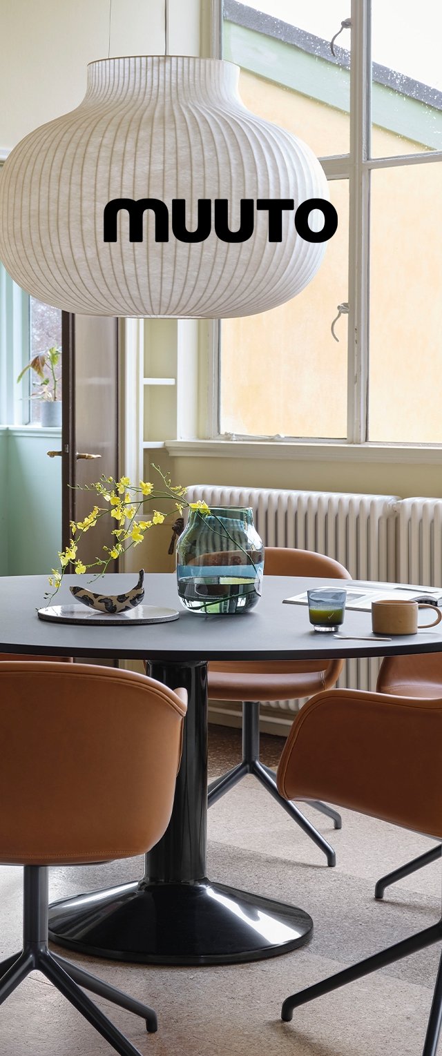 Lámpara colgante Muuto con pantalla de papel plisado blanco que cuelga sobre una mesa redonda gris. Sillas de cuero marrón alrededor y un jarrón decorativo de vidrio.