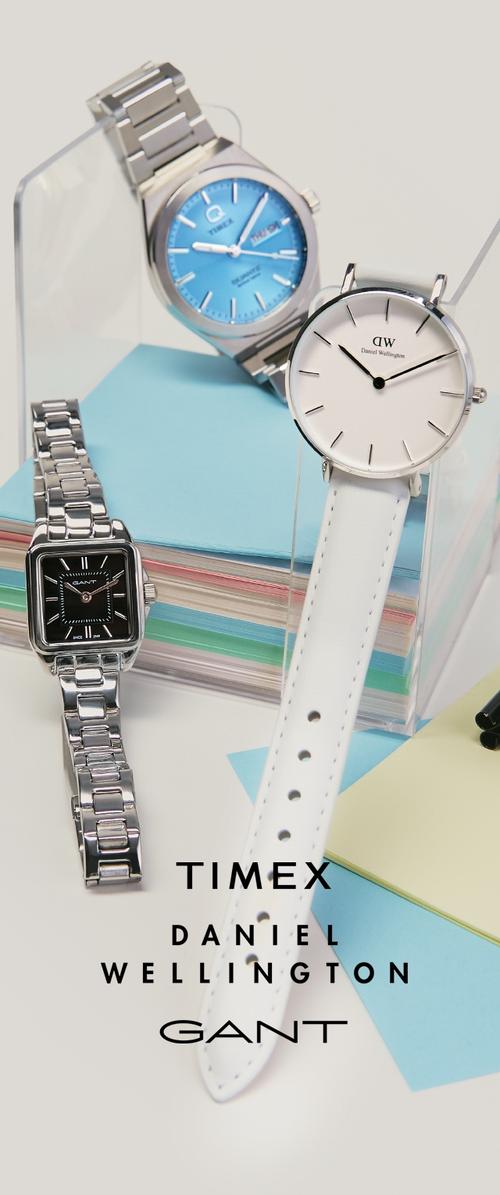 Tre handledsklockor från Timex, Daniel Wellington och Gant visade på klara ställ och färgglada staplade pappersark.